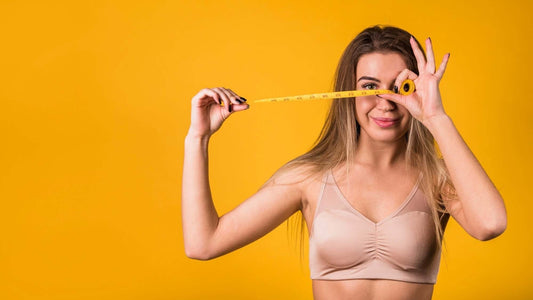 Woman in a bra measuring with a tape measure on a yellow background, demonstrating how to measure size at home.